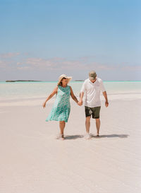 Couple walking at beach against sky