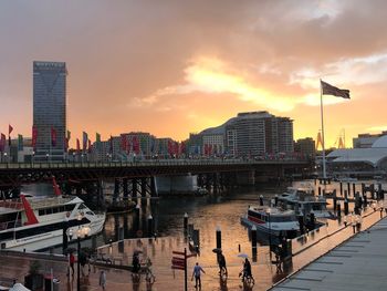 Boats in river by buildings against sky during sunset