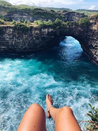 Low section of woman sitting on cliff over sea