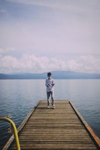 Rear view of man standing on pier over sea
