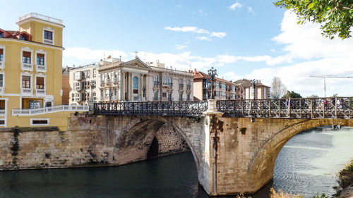 Arch bridge over river by buildings against sky