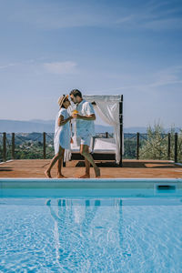 Couple standing by swimming pool against sky