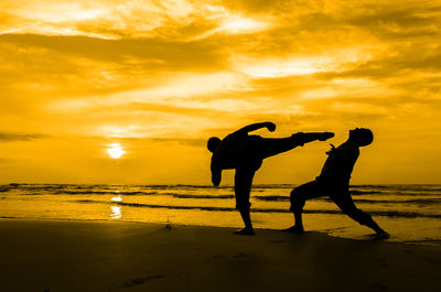 Silhouette men standing on beach against sky during sunset