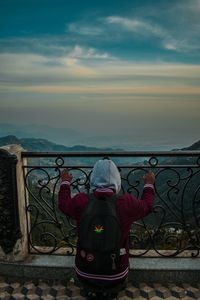 Rear view of man looking through railing against sky during sunset