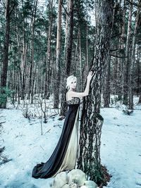 Side view portrait of female model standing by tree trunk in forest during winter