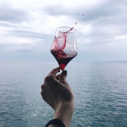 Cropped hand of woman holding drink against sea