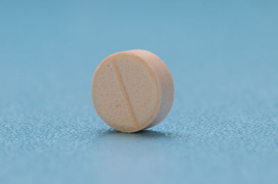 Pink tablet of medicine against light blue background, studio shot