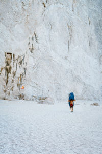 Full length of man carrying chairs while walking on sand at beach against mountain