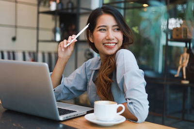 Portrait of young woman using phone while sitting at table