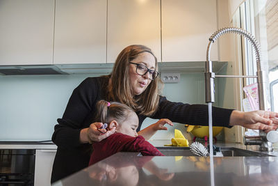 Mother helping daughter to wash hands