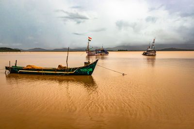 Fishing boats moored in sea against sky