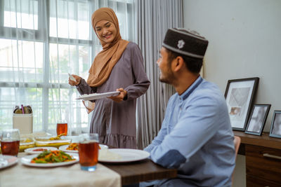 Smiling woman holding serving food to husband at home