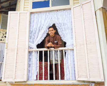 Portrait of smiling man standing by railing of window