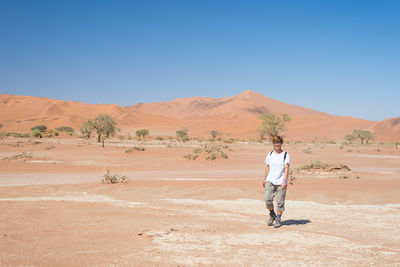 Full length of woman walking in desert against clear blue sky