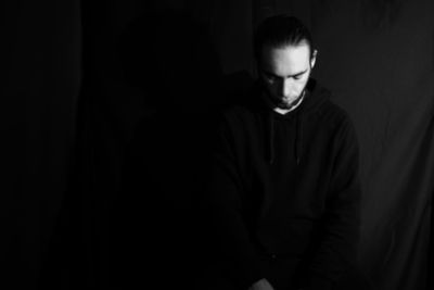 Young man looking away while standing in dark