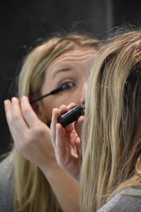 Rear view of mid adult woman applying eyeliner while looking in mirror at home