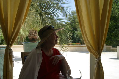 Senior woman sitting on chair amidst yellow curtains