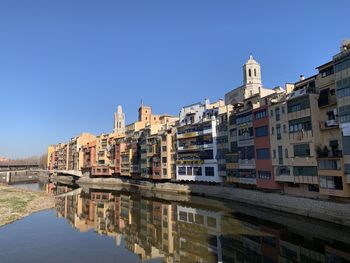 Buildings by river against clear blue sky