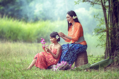 Smiling mother and daughter with flowers sitting on field