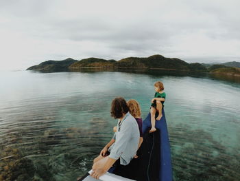 Rear view of friends standing at sea shore against sky