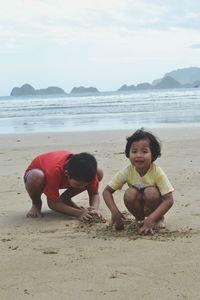 Siblings playing with sand at beach