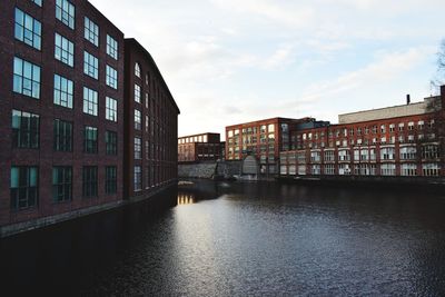 Buildings by river against sky in city