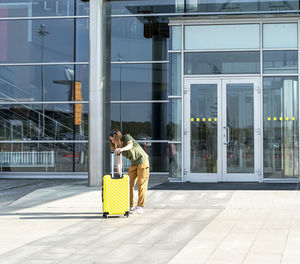 Young woman traveler carrying yellow suitcase next to entrance to airport outside tourism 