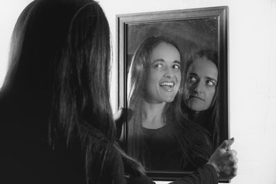 Multiple image of happy and angry woman reflected in mirror against white background