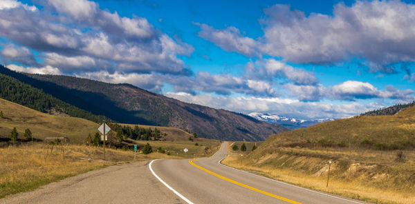 Empty road by mountain against cloudy sky