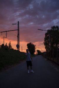 Rear view of woman on road against sky during sunset