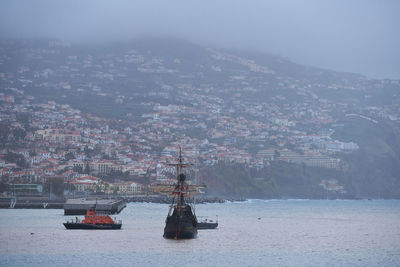 Sailboats in sea by buildings in city against sky