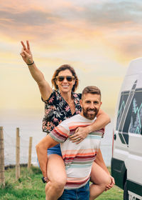 Couple looking camera having fun piggybacking next to their camper van