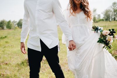 Midsection of couple with holding hands walking on field