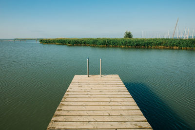 Pier over lake against clear blue sky