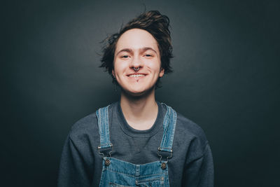 Portrait of smiling young man wearing denim overalls over gray background