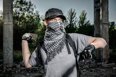 Young man wearig mask throwing stone while standing under bridge