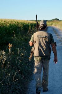 Rear view of man with gun walking on country road