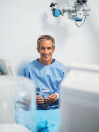 Mature man in medical uniform smiling and looking at camera while working in modern clinic