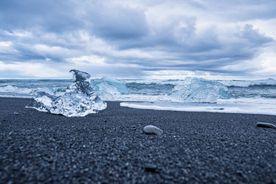 Iceberg chunks on black sand beach with waves rushing at shore against sky