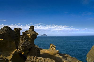 Rock formation by sea against blue sky