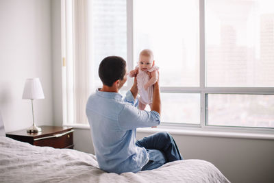 Rear view of mother and daughter on bed at home