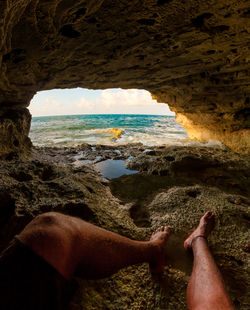 Low section of man resting in cave against sea