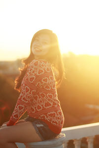 Portrait of smiling woman sitting on seat against sky during sunset