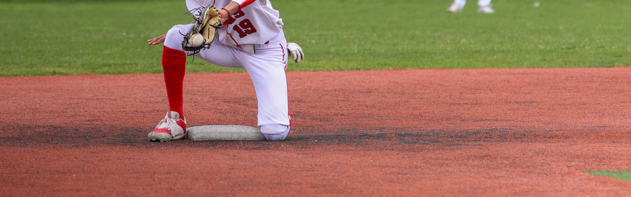 A high school baseball infielder making a play backhanding the ball over second base.