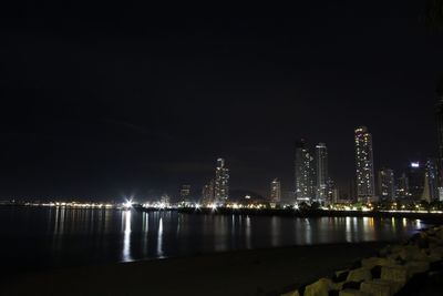 Illuminated city by river against sky at night