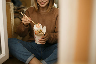 Midsection of woman eating food while sitting on floor at home