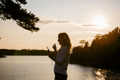 Mid adult woman talking through headphones over mobile phone at lake during sunset