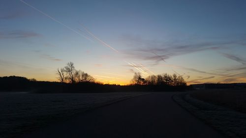 Road by silhouette trees against sky during sunset