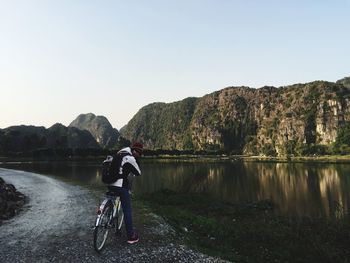 Rear view of woman with bicycle on riverbank against clear sky