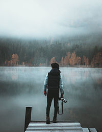 Rear view of man standing on jetty against lake